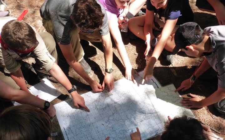 A group of students point at a map laying on the ground.